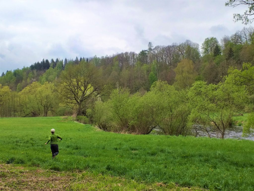 dziecko biegnące przed siebie na łące, po prawej stronie rzeka Bóbr