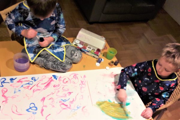 dwóch chłopców ubranych w kolorowe fartuszki maluje farbami
